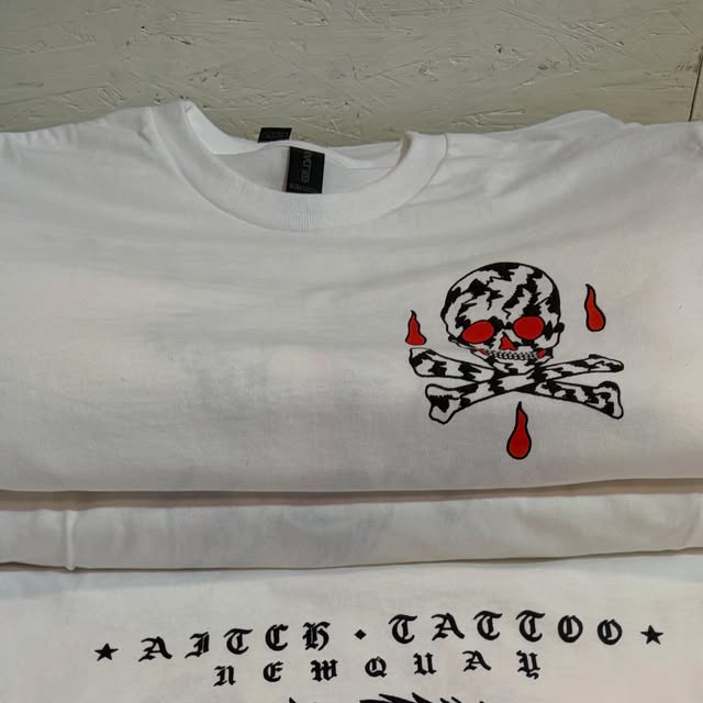 Folded white tees with a red-eyed skull and crossbones and ‘Aitch Tattoo Newquay’ in blackletter