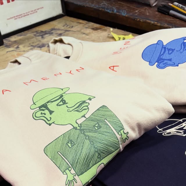 Natural sweatshirts printed with a hand-drawn green and blue baker character and the words Bara Menyn